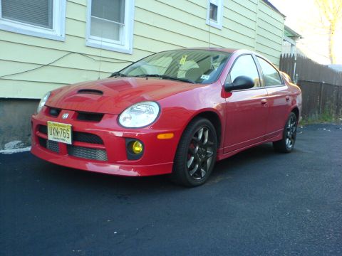 2005 Dodge SRT-4 - A red Dodge Neon SRT-4 is shown from a three-quarter front angle, parked in front of a light-colored building.