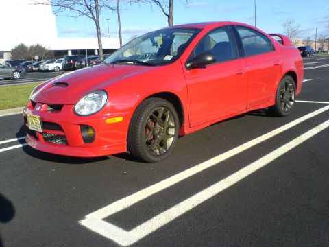 2005 Dodge SRT-4 - This red 2005 Dodge SRT-4 is captured in a three-quarter front view, parked in a lot with its distinctive hood scoop visible.