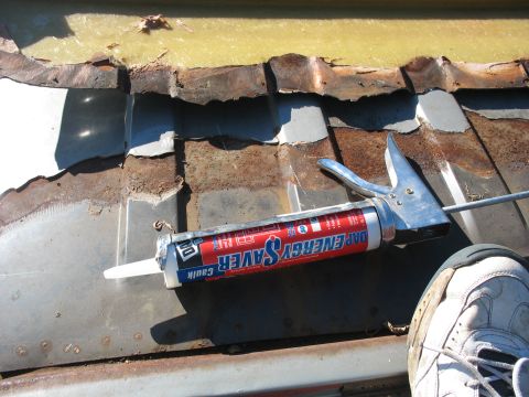 1986 Ford C-350 (Centurion Conversions) - A caulk gun rests on a heavily rusted and damaged metal surface, with a shoe in the foreground.