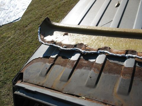1986 Ford C-350 (Centurion Conversions) - Sealant is being applied to a corroded seam on the roof of a vehicle.
