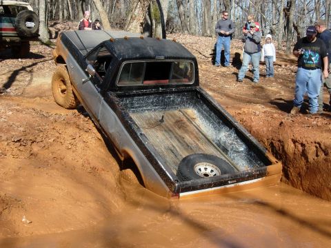 1995 Ford Bronco - A pickup truck navigates a challenging mud pit, with a spare tire visible in its bed.