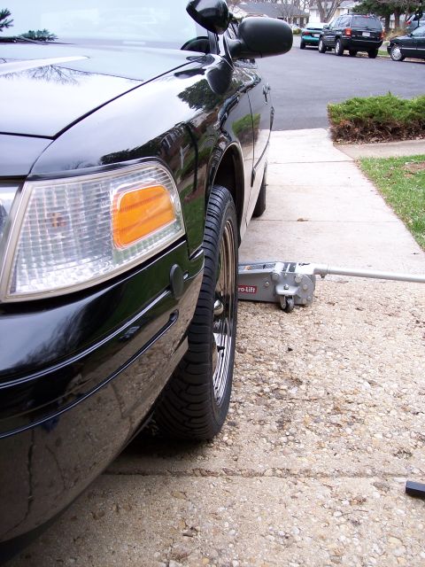 2001 Ford Crown Victoria - A black 2001 Ford Crown Victoria is shown from the front passenger side with a jack positioned under the front wheel.