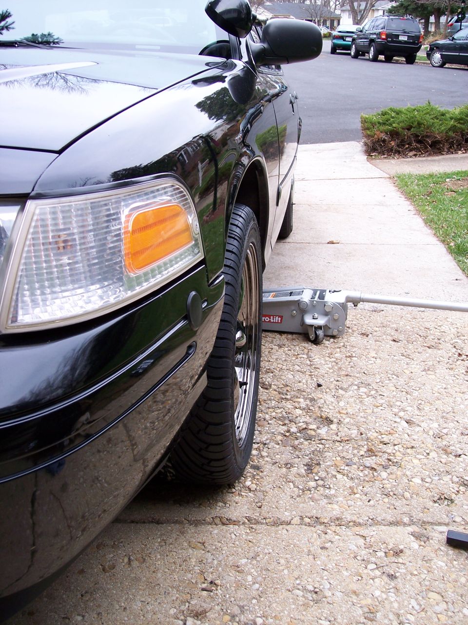 Black 2001 Ford Crown Victoria, front passenger side, jack under wheel