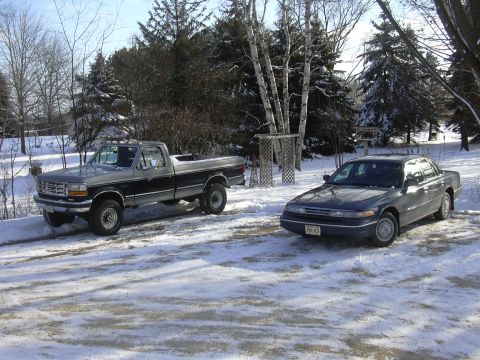 1996 Ford Crown Victoria - Two vehicles, a Ford F-Series truck and a Ford Crown Victoria, sit parked in a snowy driveway.
