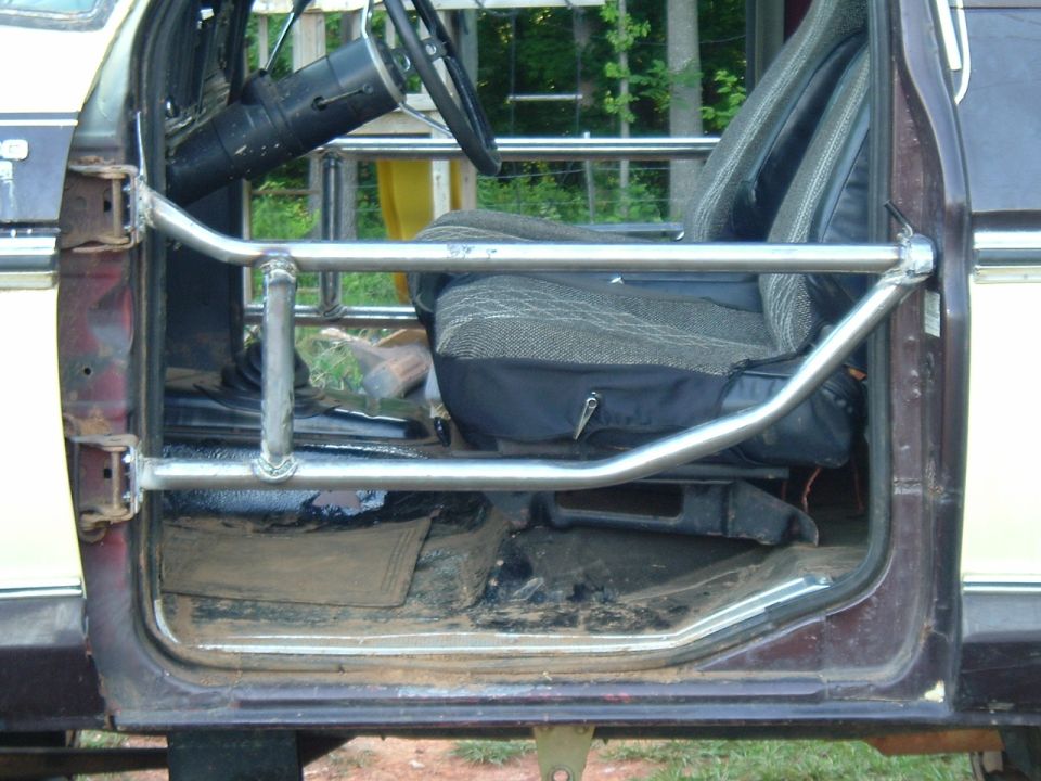 Homemade steel tube door on driver's side of a dark pickup, interior seat and steering wheel visible