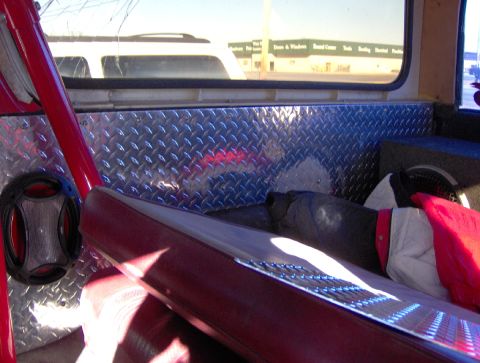 1978 Ford Bronco - Interior shot behind the red vinyl bench seat of a truck, with the rear cargo area walls fully lined in diamond-plate aluminum and a round…