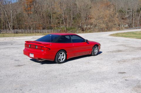 1996 Ford Probe - A red 1996 Ford Probe is parked on a gravel lot with trees in the background.