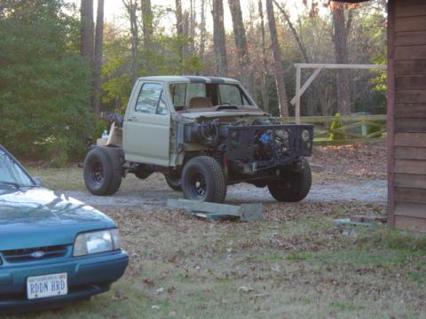 1991 Ford Bronco - A pickup truck is undergoing repairs in a yard, with its front end removed and engine visible.