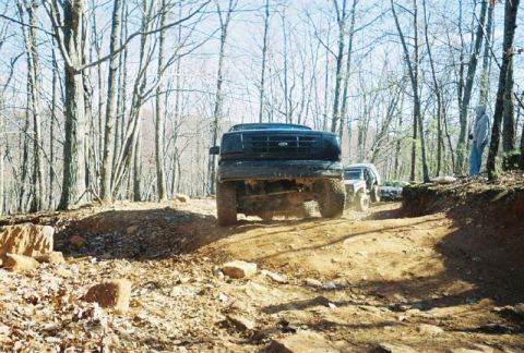 1993 Ford Bronco - Off-road vehicles navigate a wooded trail with rocky terrain.