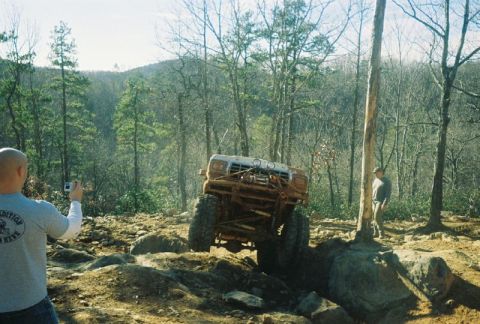 1993 Ford Bronco - A heavily modified off-road vehicle navigates a rocky terrain, with a spectator observing and filming.