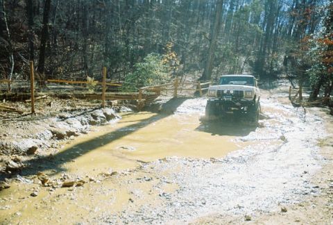 1993 Ford Bronco - Modified Ford Bronco navigates a muddy trail with large tires.