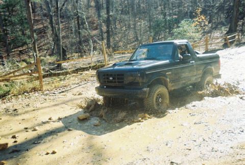 1993 Ford Bronco - A 1993 Ford Bronco navigates a muddy trail in a wooded area.