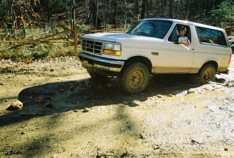 1993 Ford Bronco - A white 1993 Ford Bronco navigates a muddy trail, kicking up dirt and water.