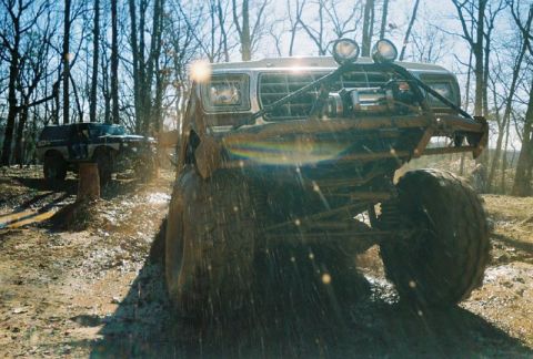 1993 Ford Bronco - Two SUVs navigate a muddy trail through a wooded area on a sunny day.