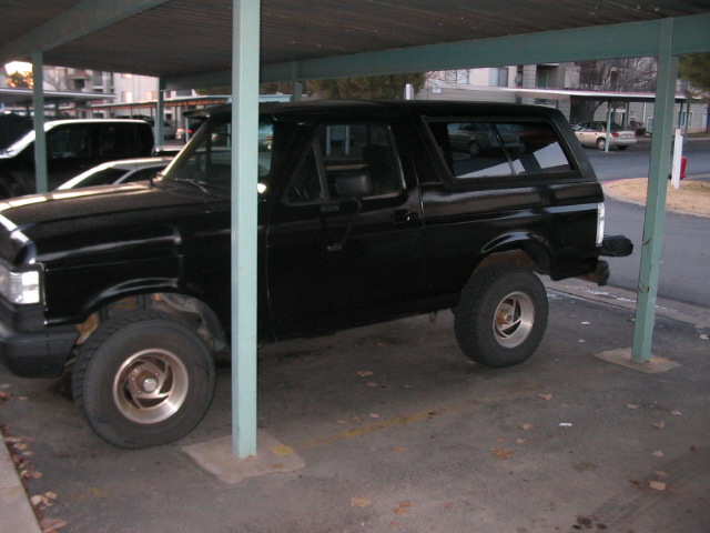 Black SUV parked under a carport, side view, showing its front and rear tires and windows