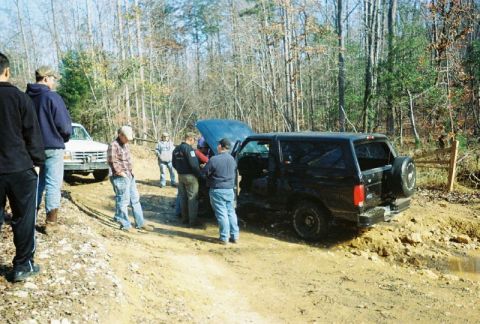 1993 Ford Bronco - A group of people inspect a black 1993 Ford Bronco that appears to be stuck in the mud with its hood open.
