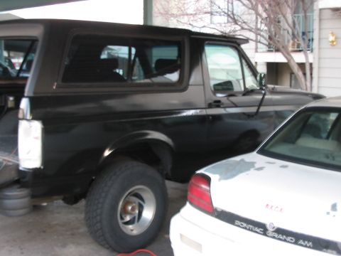 1991 Ford Bronco - A black Ford Bronco is parked next to a white Pontiac Grand Am, with the Bronco's rear tire visible.
