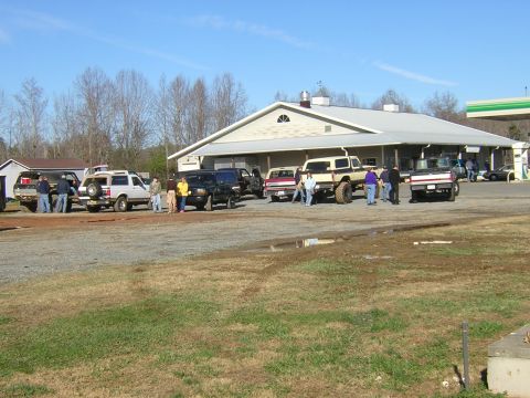 1979 Ford Bronco - A gathering of trucks and SUVs in a parking lot outside a building with gas pumps visible in the background.