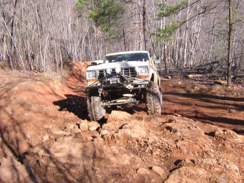 1979 Ford Bronco - A modified off-road vehicle tackles a challenging, rocky path through a wooded area.