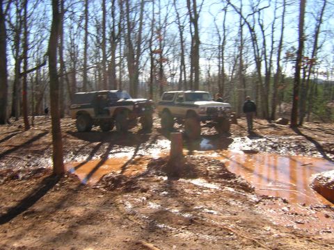 1979 Ford Bronco - Two off-road vehicles navigate a challenging muddy terrain in a forest setting.