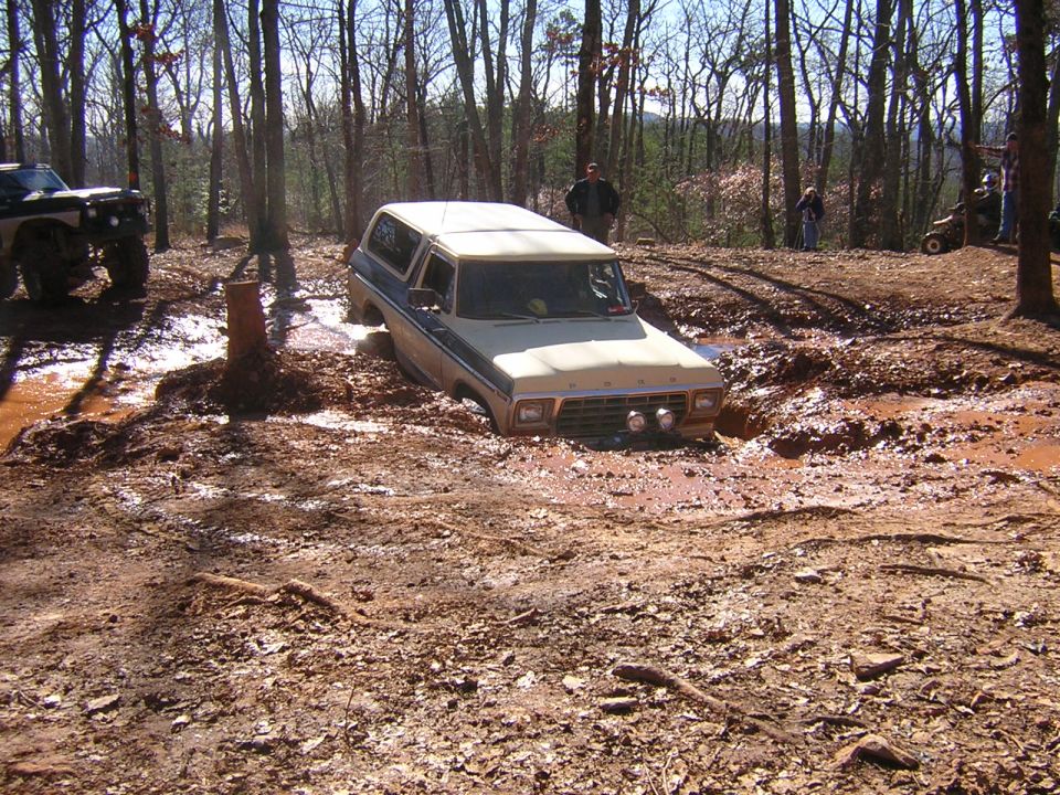 Tan and blue Ford Bronco stuck in deep mud, front view