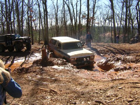 1979 Ford Bronco - Two off-road vehicles navigate a muddy trail in a wooded area during an event.