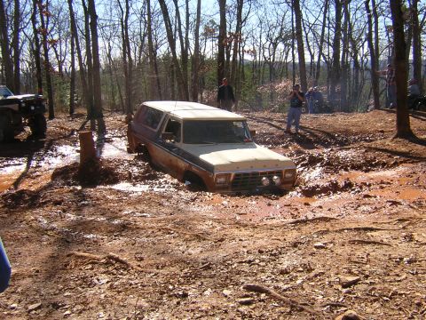 1979 Ford Bronco - An off-road event shows a vintage Ford Bronco deeply mired in a muddy woodland path.