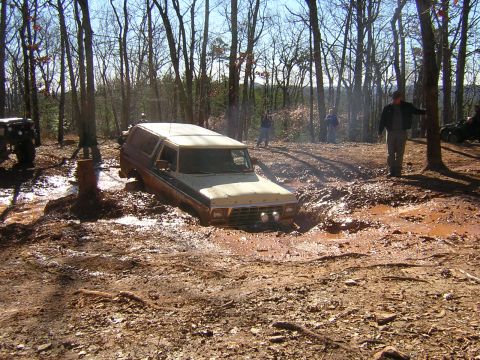 1979 Ford Bronco - A Ford Bronco is stuck in a muddy trail surrounded by trees, with another vehicle nearby.