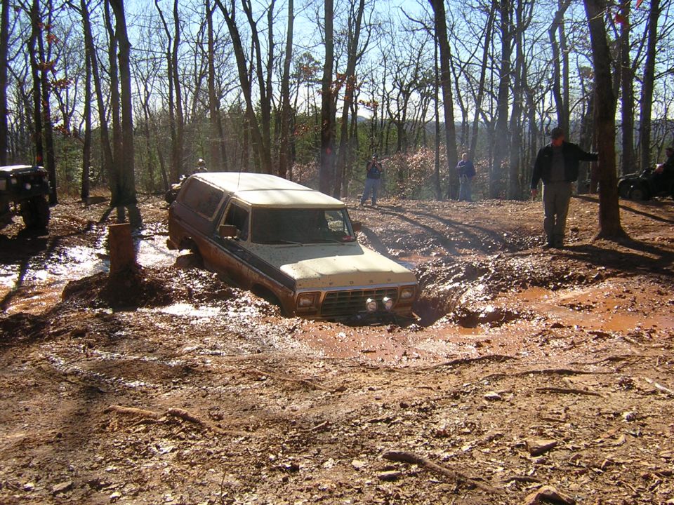 Ford Bronco stuck in mud on a wooded trail. Another vehicle is visible to the left