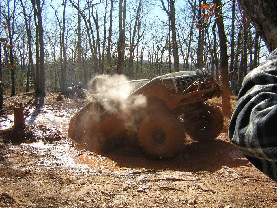 1979 Ford Bronco stuck in mud, kicking up dust. Another ATV visible in background