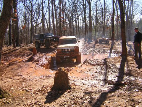 1979 Ford Bronco - Off-road vehicles navigate a challenging muddy course in a wooded area.