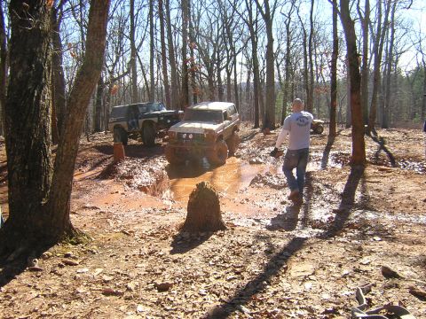 1979 Ford Bronco - Off-road vehicles tackle a challenging muddy course amidst a wooded area.