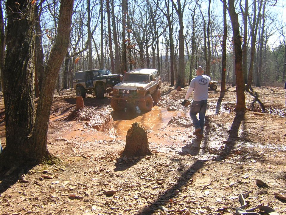 Two off-road SUVs navigating a muddy trail in a forest, one white and one dark colored