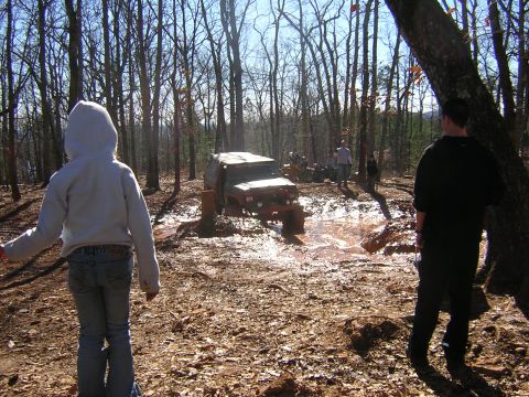 1979 Ford Bronco - An off-road vehicle tackles a challenging muddy path during an outdoor event in a forest.