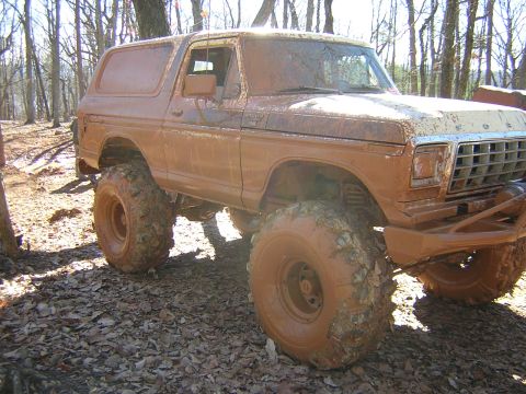1979 Ford Bronco - A heavily mud-splattered 1978 Ford Bronco sits in a wooded area, its large tires caked with dirt.