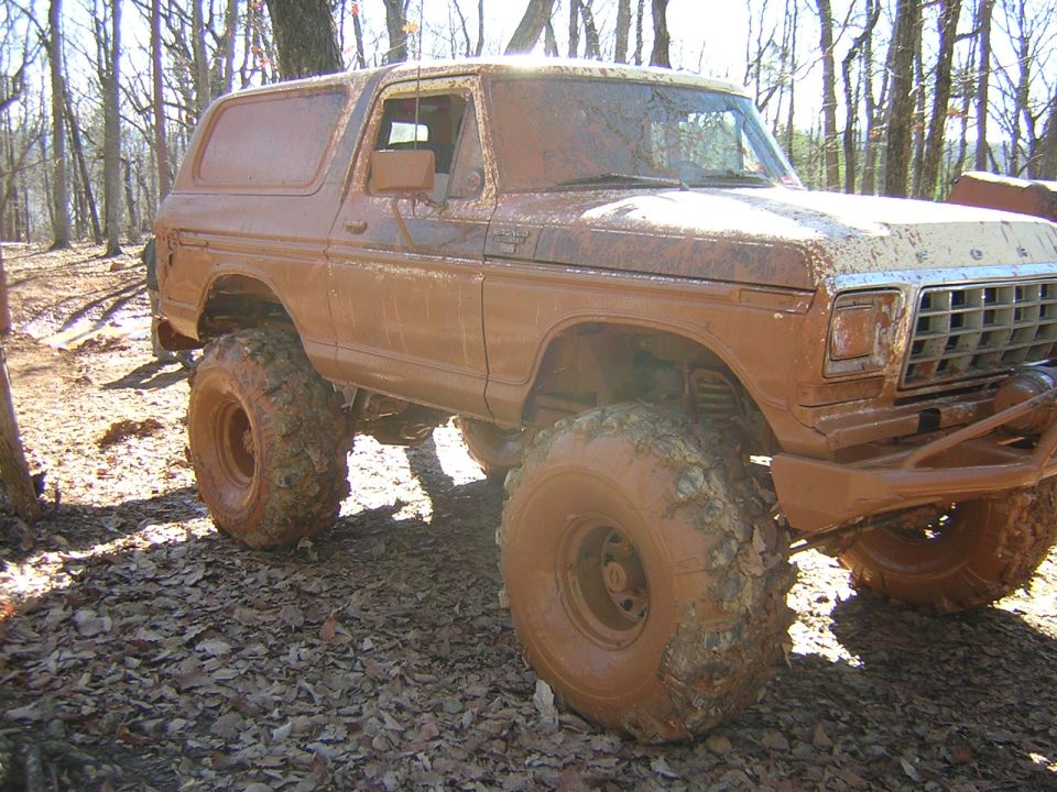 Mud-covered 1978 Ford Bronco with large off-road tires, viewed from the front three-quarter angle
