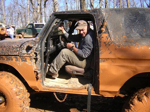 1979 Ford Bronco - A man sits in the driver's seat of a heavily mud-covered off-road vehicle, with other vehicles in the background.