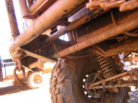 1979 Ford Bronco - Close-up view of the heavily mud-caked chassis and suspension of an off-road vehicle, with another vehicle partially visible in the backgro…