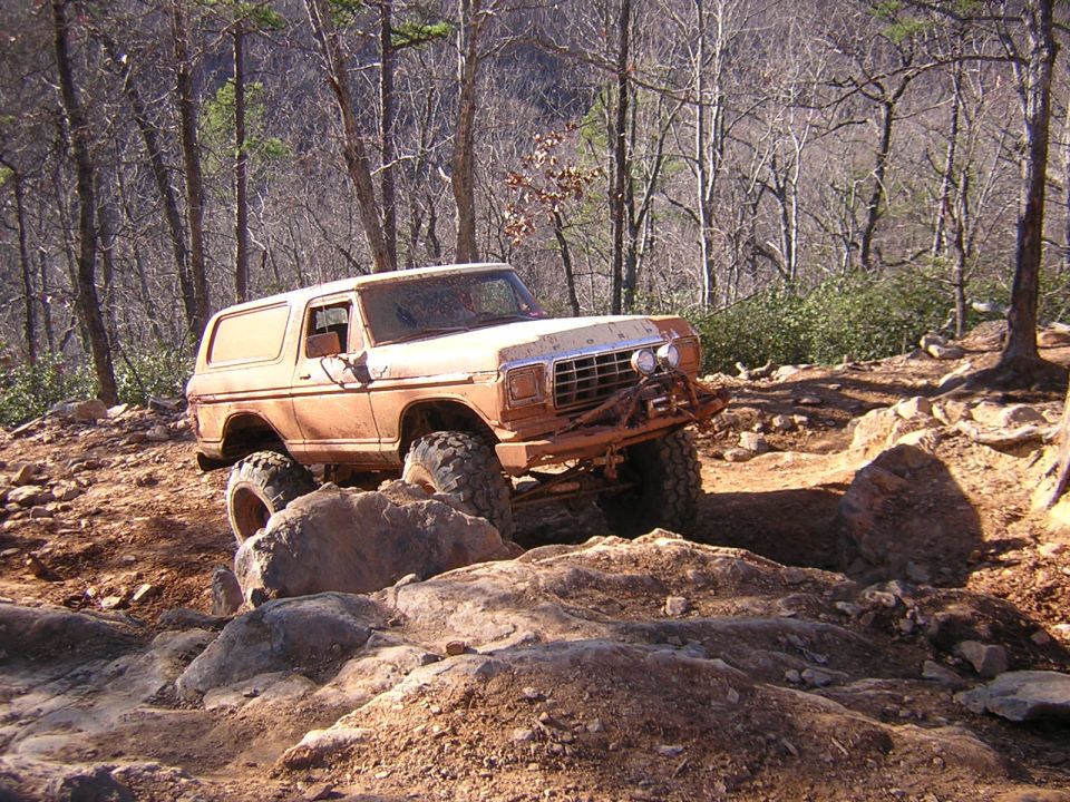 Orange off-road SUV climbing over rocks on a dirt trail