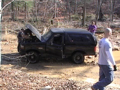 1979 Ford Bronco - A black Ford Bronco appears to be stuck in the mud in a wooded area, with people attending to it.