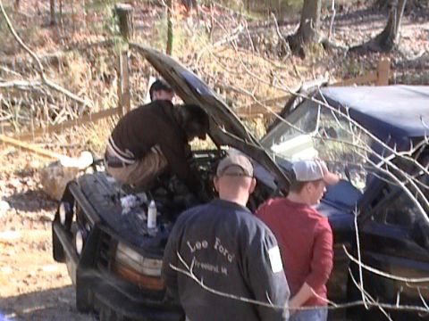 1979 Ford Bronco - Men attend to the engine of a black Ford Bronco with its hood open in a wooded area.