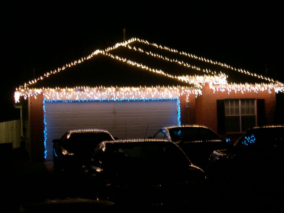 House decorated with Christmas lights, multiple cars parked in driveway at night