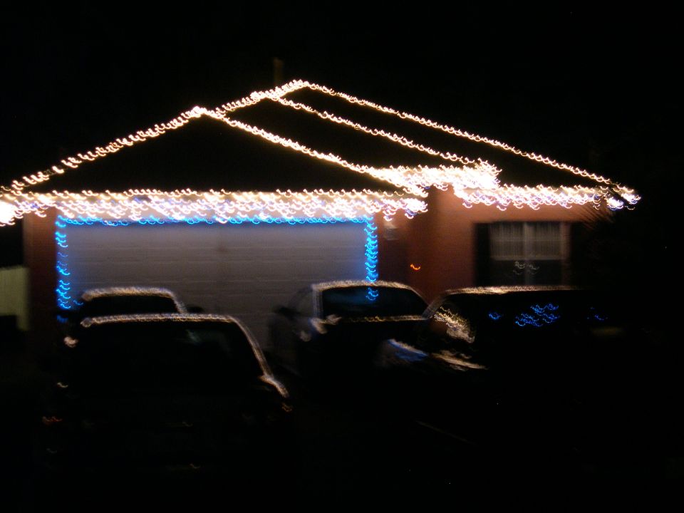 Cars parked in front of a house with Christmas lights on the roofline