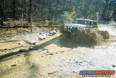 1992 Ford Mustang - A white Ford Bronco navigates a muddy trail, kicking up a large spray of mud and water.