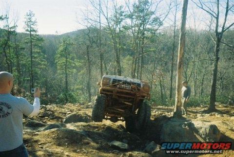 1992 Ford Mustang - A modified off-road vehicle navigates a challenging rocky terrain in a wooded area.