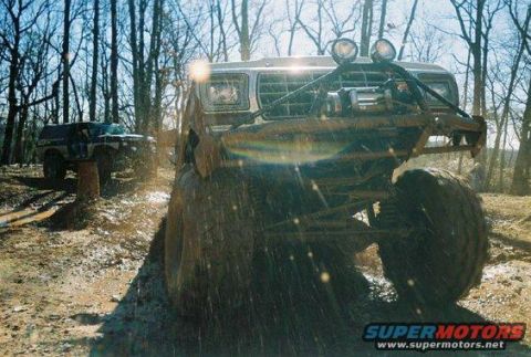1992 Ford Mustang - Two off-road vehicles navigate a muddy trail through a wooded area.