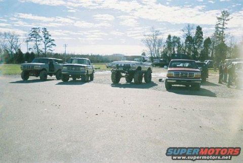 1992 Ford Mustang - Several lifted trucks and SUVs are parked outdoors under a partly cloudy sky.