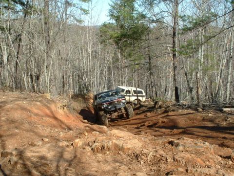 1992 Ford Mustang - Two off-road vehicles navigate a challenging dirt path through a wooded area.