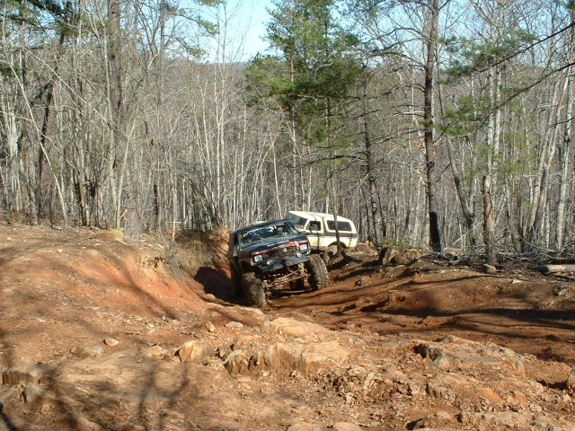 Black off-road SUV climbing a steep, rocky dirt trail with a white camper van behind it