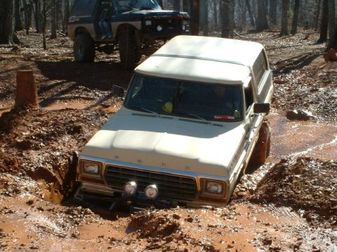 1992 Ford Mustang - A tan Ford Bronco is stuck in a muddy ditch, with another off-road vehicle behind it.
